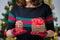 Woman hodling two gift boxes in hands, one bigger and one smaller. Christmas tree with decoration and lights blur in background.