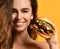 Woman hold big beef cheeseburger sandwich with hungry mouth happy smiling on yellow backgroun