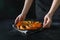 Woman hold slice of pumpkin roasted with thyme and salt. Dark style. Close up