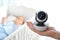 Woman holding baby camera near crib with child in room.