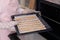 Woman holding baking sheet with homemade breadsticks near oven in kitchen, closeup. Cooking traditional grissini