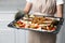 Woman holding baking tray with sea bass fish and vegetables in kitchen, closeup