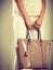 Woman holding beige lacquered leather bag.