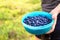 Woman holding blueberries in a casket and container in forest.