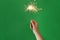 Woman holding bright burning sparkler on green background, closeup