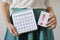 Woman holding calendar with marked missed period and exclmation mark. Unwanted pregnancy and delay in menstruation.