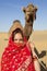 Woman holding a camel in the desert.