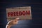 Woman holding cardboard paper with FREEDOM text and rusty sharp bare wire on dark background, conceptual image