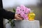 Woman holding chrysanthemum flowers near granite tombstone with candle outdoors, closeup. Funeral ceremony