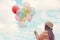 Woman holding colorful balloons and flying on clouds sky background