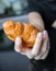 Woman holding a croissant in her hand, closed up