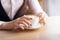 Woman holding cup of capuccino on wooden table.