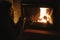 Woman holding cup of tea and warming up hands at cozy fireplace in dark evening room. Fireplace heating in house, electricity