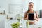 Woman holding digital tablet with blank screen near blender and glass with smoothie