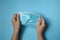 Woman holding disposable face mask on blue background, closeup. Protective measures during coronavirus quarantine