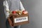 Woman holding donation box with food on gray background