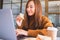 A woman holding and eating whole wheat sandwich while working on laptop computer