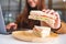 A woman holding and eating whole wheat sandwich while working on laptop computer