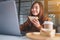 A woman holding and eating whole wheat sandwich while working on laptop computer