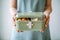 A woman holding a green lunch box filled with food. Generative AI image.