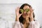 Woman holding halves of kiwi fruit while covering eyes