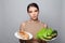 Woman holding in hand sandwich and vegetables choosing, trying to resist temptation, making the right dietary choice