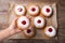 Woman holding Hanukkah doughnut with jelly and sugar powder over wooden table, top view