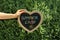 Woman holding heart shaped blackboard with text SUMMER CAMP and drawing near green bush