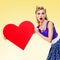 Woman holding heart symbol, pin up style, yellow background