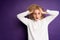 woman holding her head with two hands ruining her hair in a white sweater on a purple background