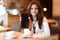 Woman holding her smartphone showing device during lunch break drinking hot coffee in trendy cafe looking happy modern