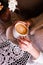 Woman holding hot cup of coffee. A girl in cafe with beige nails is holding a cup with cappuccino with a pattern