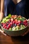 A woman holding a large vibrant smoothie bowl loaded with berries, kiwi, yogurt and seeds