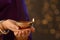 Woman holding lit diya lamp in hands against blurred lights, closeup. Diwali celebration