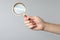 Woman holding magnifying glass on grey background, closeup. Find keywords concept