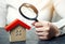 A woman is holding a magnifying glass over a wooden house. Real estate appraiser. Assessment of the condition of the house.