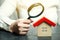 A woman is holding a magnifying glass over a wooden house. Real estate appraiser. Assessment of the condition of the house.