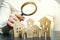 A woman is holding a magnifying glass over a wooden houses. Real estate appraiser. Property valuation / appraisal. Find a house.