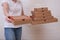 Woman holding many stacked carton pizza boxes of different sizes and offering, giving one to a customer, restaurant delivery