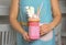 Woman holding mason jar of tasty milk shake with sweets indoors