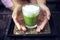 Woman holding Matcha green tea latte on wooden table