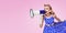 Woman holding megaphone, in pin-up style. Copy space. Pink background. Caucasian blond model in retro fashion, vintage