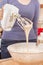 Woman is holding a mixer. Dough flows into the bowl from the mixer blades. Preparing baking by a woman.