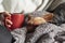 Woman holding a mug with hot beverage and covered with warm blanket with her pet