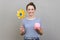 Woman holding origami hand mill on stick and piggy bank, looking at camera with happy expression.