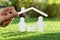 Woman holding paper roof over cutout of family on fresh grass, closeup. Life insurance