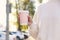 Woman holding pink takeaway cardboard cup on city street, closeup. Coffee to go