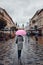 Woman holding pink umbrella walking in a downtown on rainy gloomy autumn day