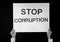 Woman holding placard with text STOP CORRUPTION on dark background, black and white effect