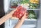 Woman holding plastic bag with frozen tomatoes near open refrigerator